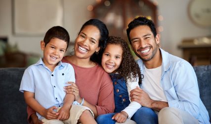 Portrait of smiling mixed race family relaxing together on sofa at home. Carefree loving hispanic parents bonding with cute little son and daughter. Happy kids spending quality time with mom and dad