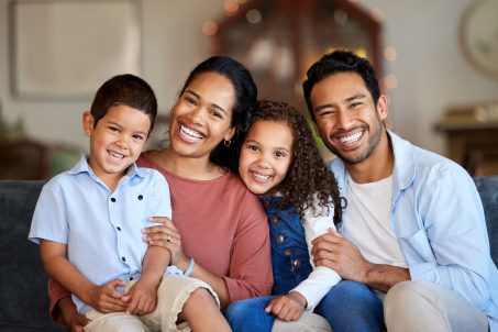 Portrait of smiling mixed race family relaxing together on sofa at home. Carefree loving hispanic parents bonding with cute little son and daughter. Happy kids spending quality time with mom and dad